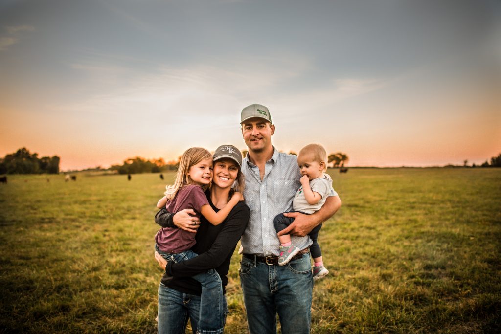 a family unit of a mom, dad and two girls stands in a pasture